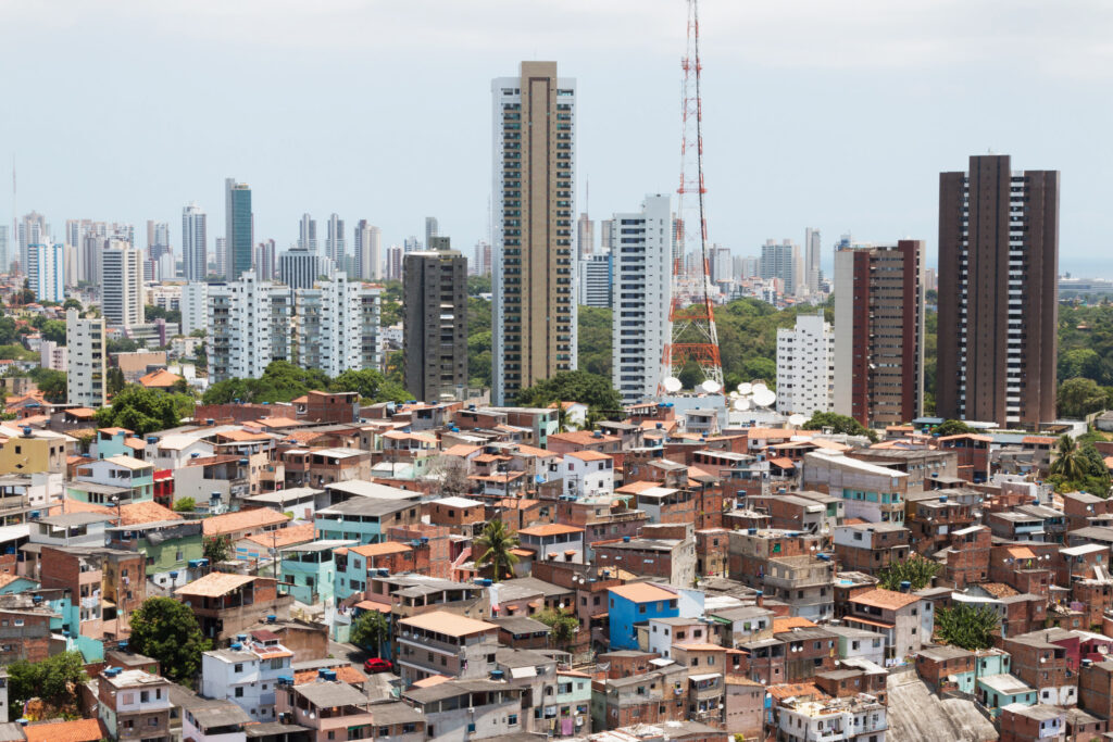 Imagem mostra casas de baixa renda à frente e prédios e uma antena de TV ao fundo